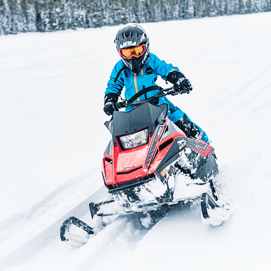 Un jeune pilote conduit sa motoneige dans un sentier de neige